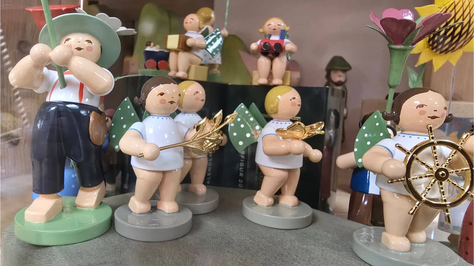 Mehrere bemalte Holzfiguren mit grünen Flügeln, goldenen Details und unterschiedlichen Frisuren auf runden Sockeln