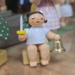 Kleine Holzfigur mit weißem Kleid, blauem Muster, goldenem Glöckchen und weißem Schwert