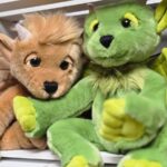 Zwei Drachen-Plüschtiere, eines braun mit Hörnern und eines grün mit Flügeln und gelben Details