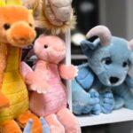 Mehrere Drachen-Plüschtiere in Orange, Pink und Blau mit unterschiedlichen Kopfformen