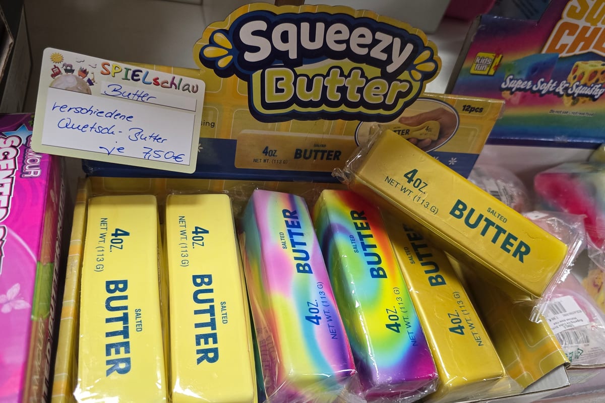 Squeezy Butter in Gold, gelb und in Regenbogenfarben, gestapelt im Regal bei SPIELschlau in Jena Squeezy Butter in Gold, gelb und in Regenbogenfarben, gestapelt im Regal bei SPIELschlau in Jena